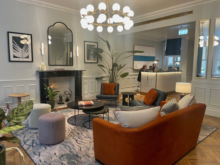 The reception area featuring an amber coloured sofa, statement light, light walls and reception desk