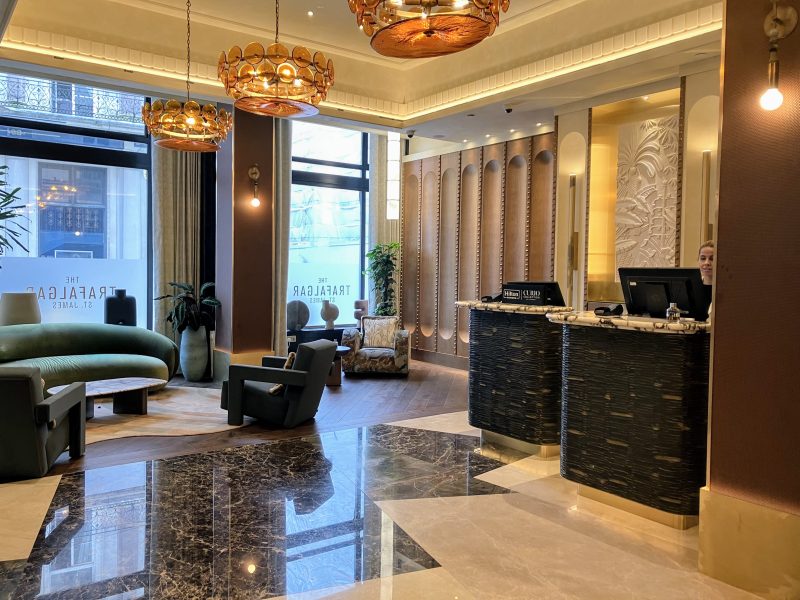 The reception area featuring black and white marble adjacent to a wooden floor, seating area including a deep green sofa and three pendant lights.