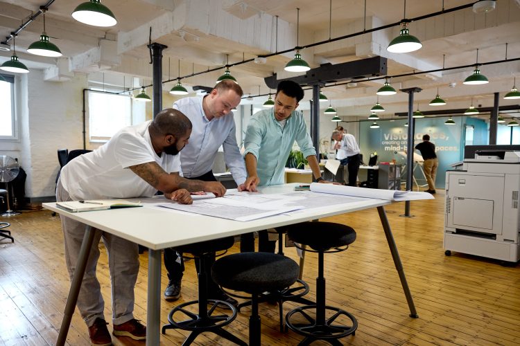 Sef, Mike and Josh stood around the collaboration table in the studio looking at some drawings