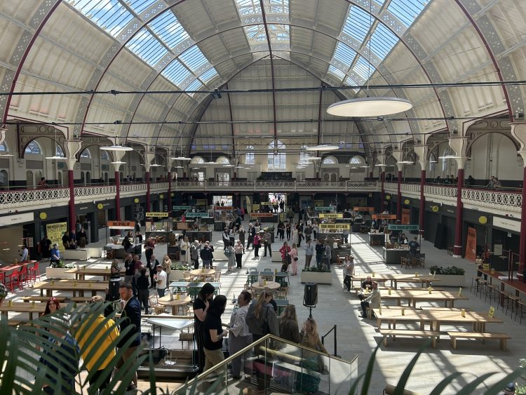 Derby Market Hall - a large open space with an arched roof and skylights. Inside, there are street food vendors and shops at the sides with large wooden tables and benches in the middle