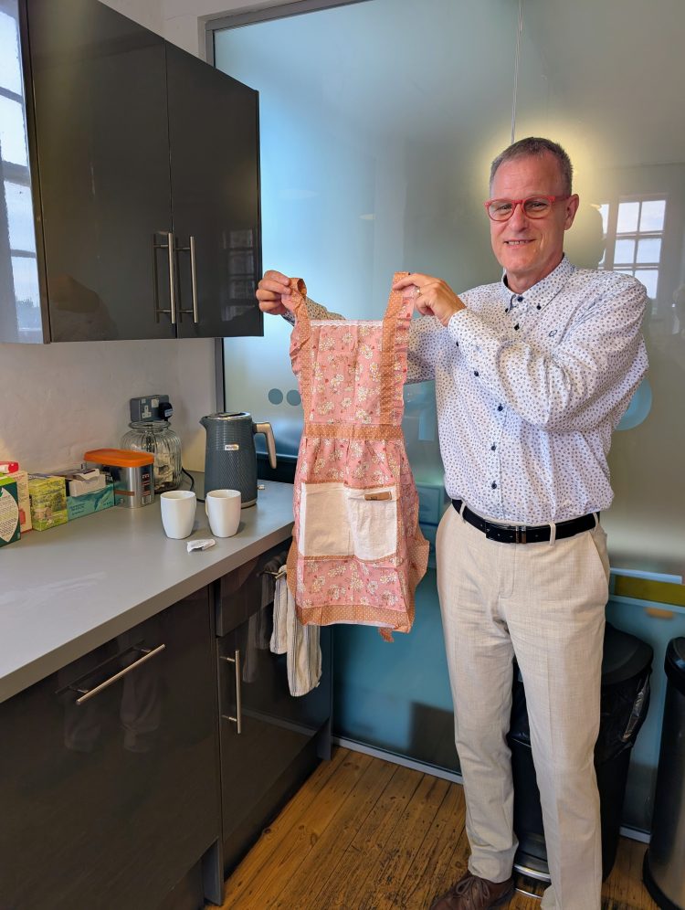 Dale Roberts pictured in our studio kitchen, holding up a pink frilly apron