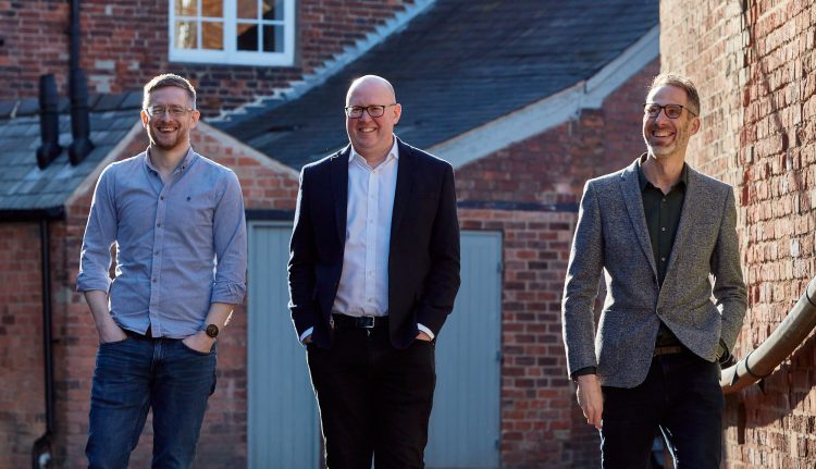 Directors David Gardner, Peter Newman-Earp and Nik Clarke walking together with the red brick mill buildings in the background.