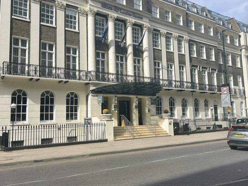 Street view of Hilton Euston - an historic building with columns, arched windows and flags.