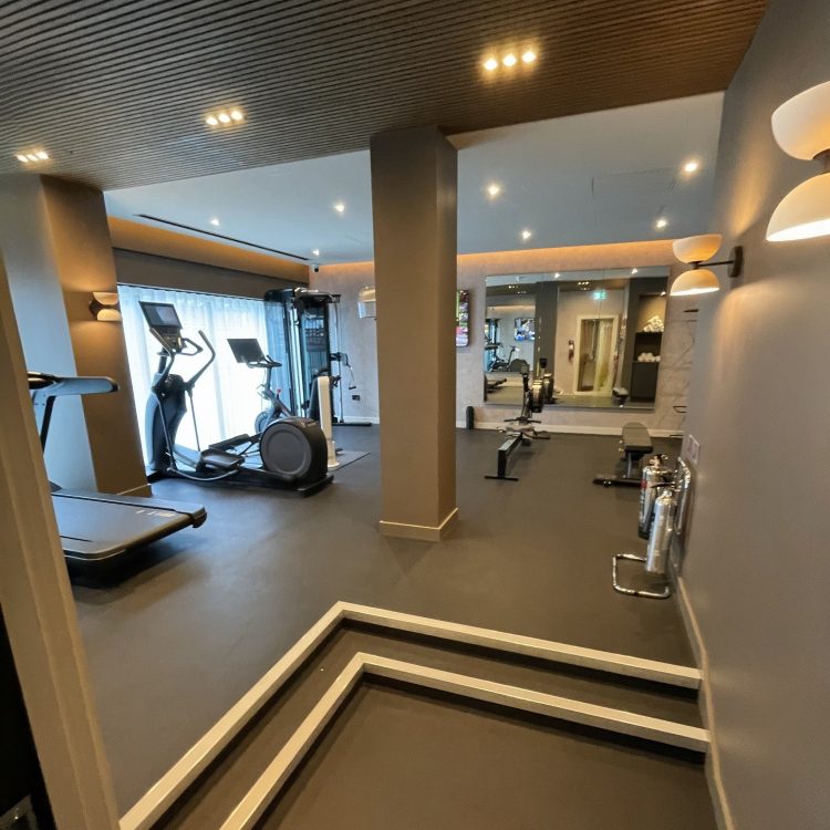 A photograph of the new gym. Modern gym interior with exercise machines, treadmills, and a workout bench under soft lighting. The space is clean and inviting with a calm ambiance and grey flooring.