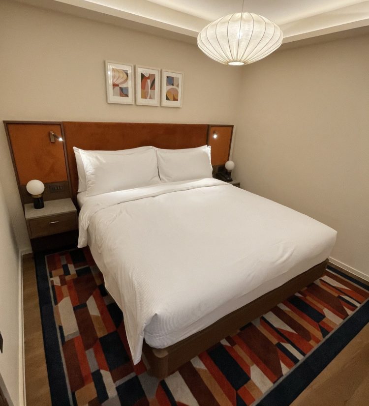 One of the new guest bedrooms featuring a double bed, white linens, abstract art above the headboard, and a pendant light. The colorful rug adds warmth.