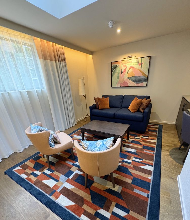 A cosy living area of the duplex suite featuring a blue sofa with orange cushions, two stylish armchairs, and a geometric patterned rug under soft lighting.