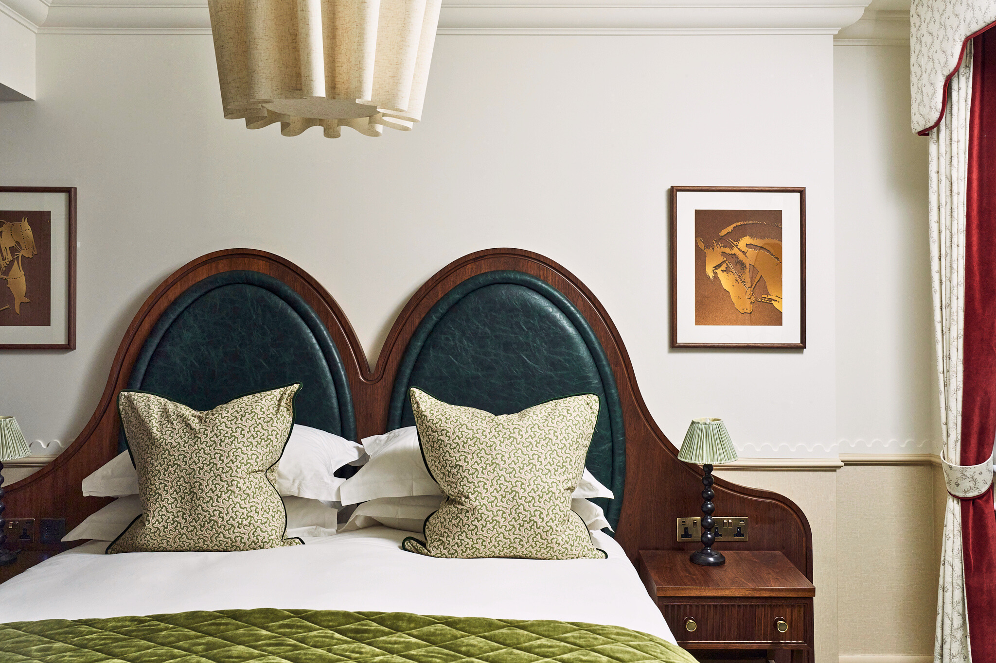 Stylish bedroom with a dark wood and green upholstered headboard. White bedding, patterned pillows, green quilt, framed art, and a warm ambiance.