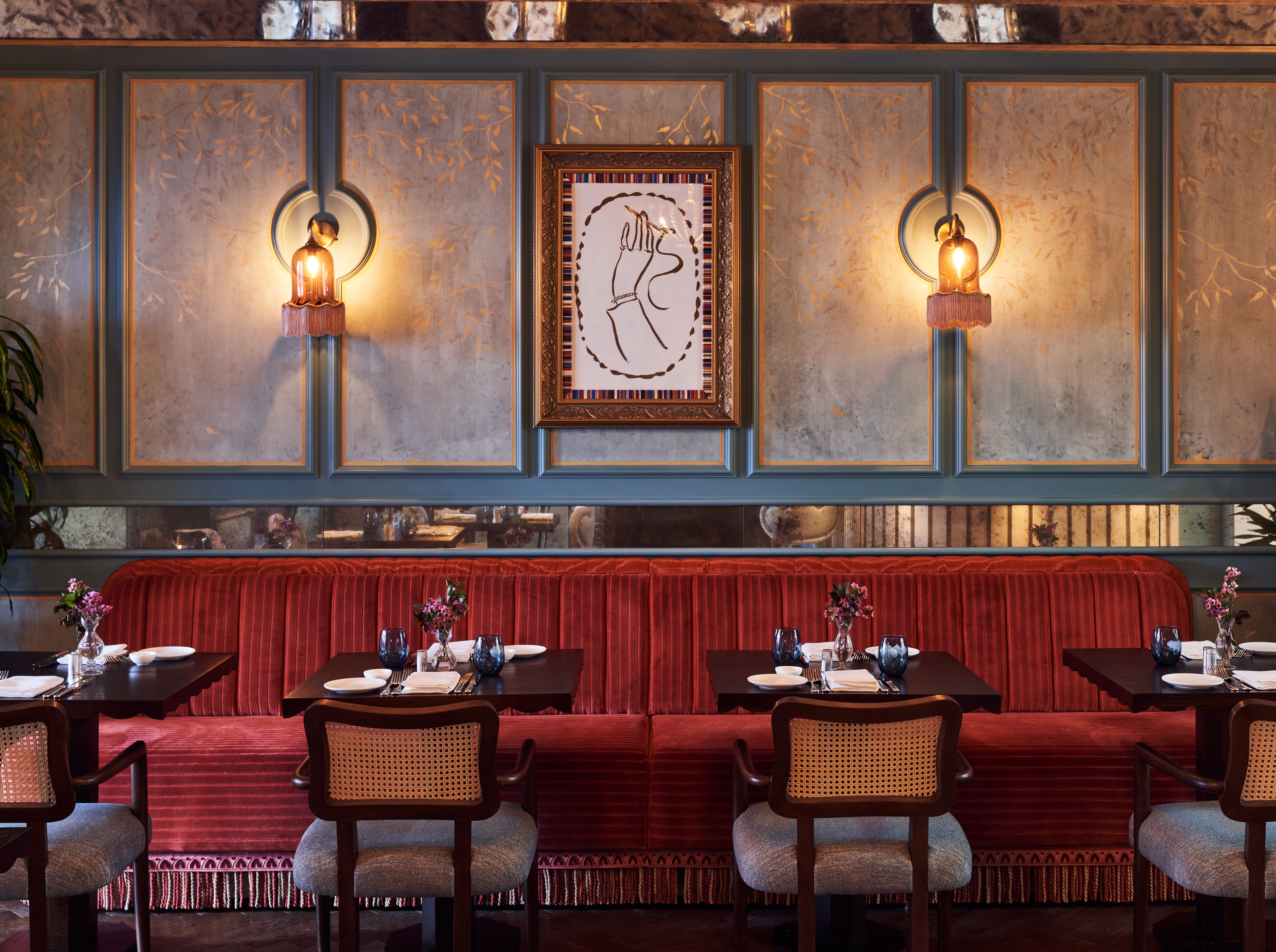 Restaurant seating area with red strip bench seat, panelled walls with gold leaf pattern and accent wall lights.