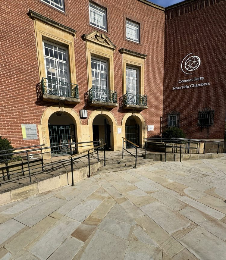 External photo of Riverside Chambers with stone paving, black and brass handrails and the red brick building with large windows behind