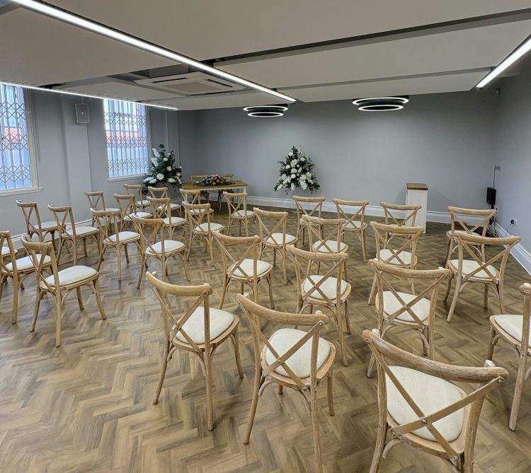 Photo of the ceremony room with wooden floor, looking to the front at the room which has feature circular lighting and floral displays