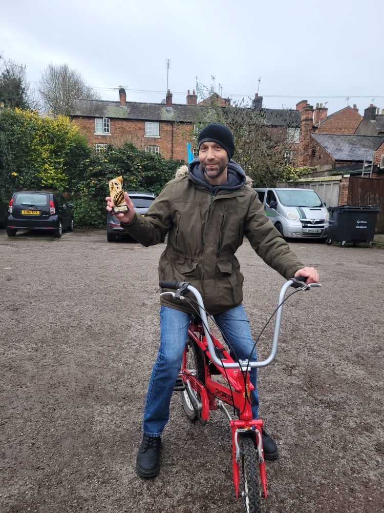 John on hie Raleigh Chopper holding up a trophy after his charity challenge in 2024