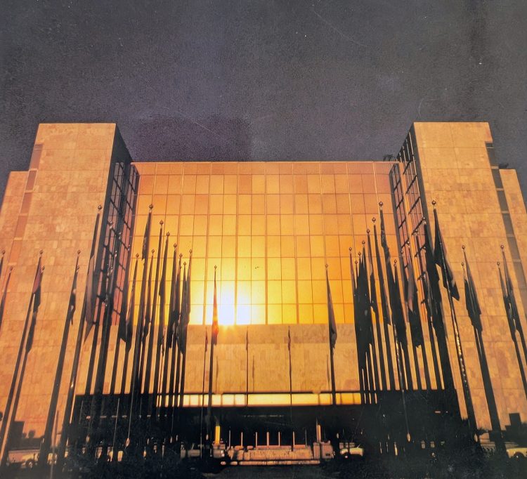 The sun reflecting a golden light off the front mirrored facade. There are lots of tall flags at the front of the hotel.