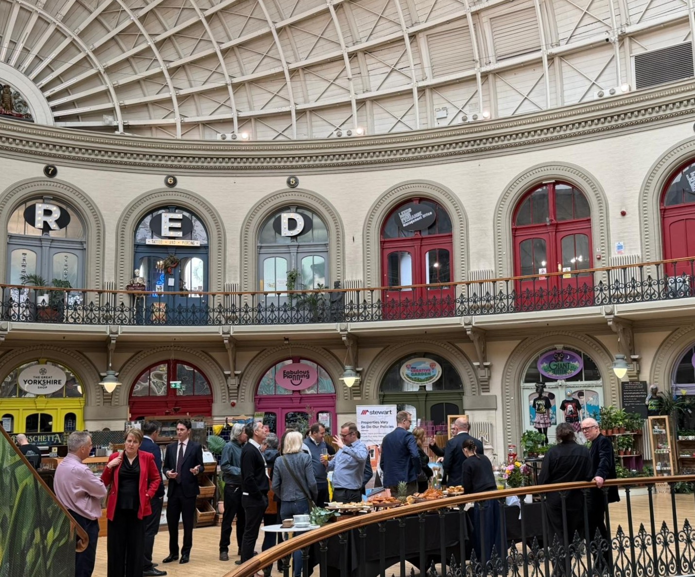 Photo from inside Leeds Corn Exchange. It has a tall, domed roof, a mezzanine level and lots of people networking on the lower level at UKREiiF