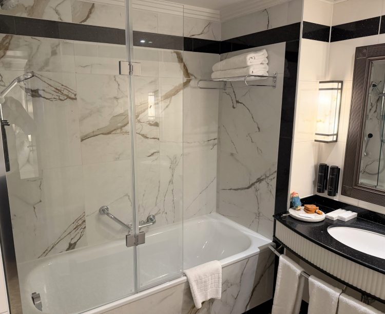 Monochrome bathroom with marble over the bath and shower area. Black counter on the sink with Paddington bear bath bombs on the side.