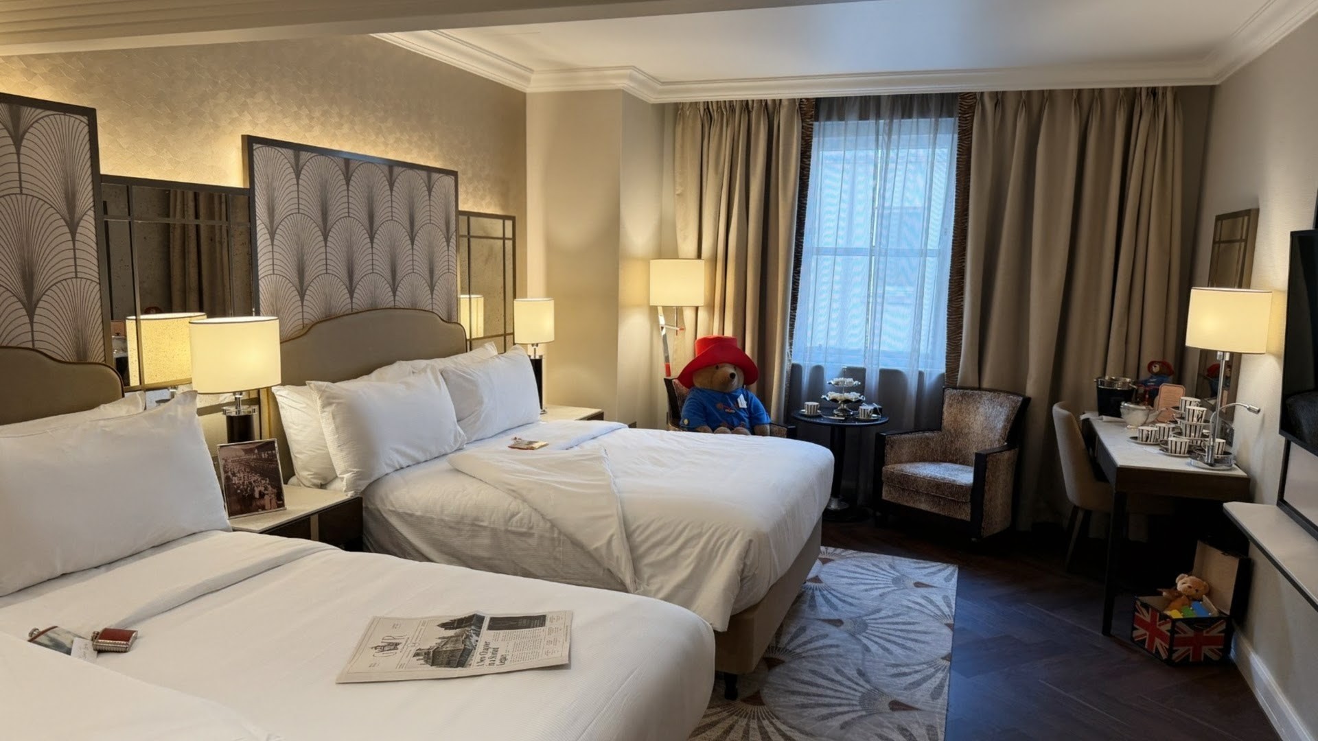 A stylish guest bedroom with two double beds featuring Paddington bear and a newspaper on the bed.