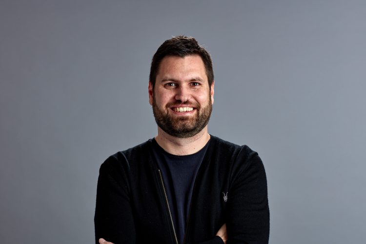 James Parratt smiling at the camera in front of a grey background.