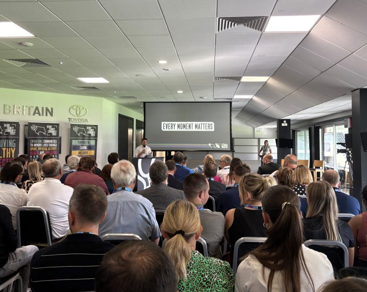 A photograph of a room at Pride Park full of people seating looking at a screen where someone is presenting.
