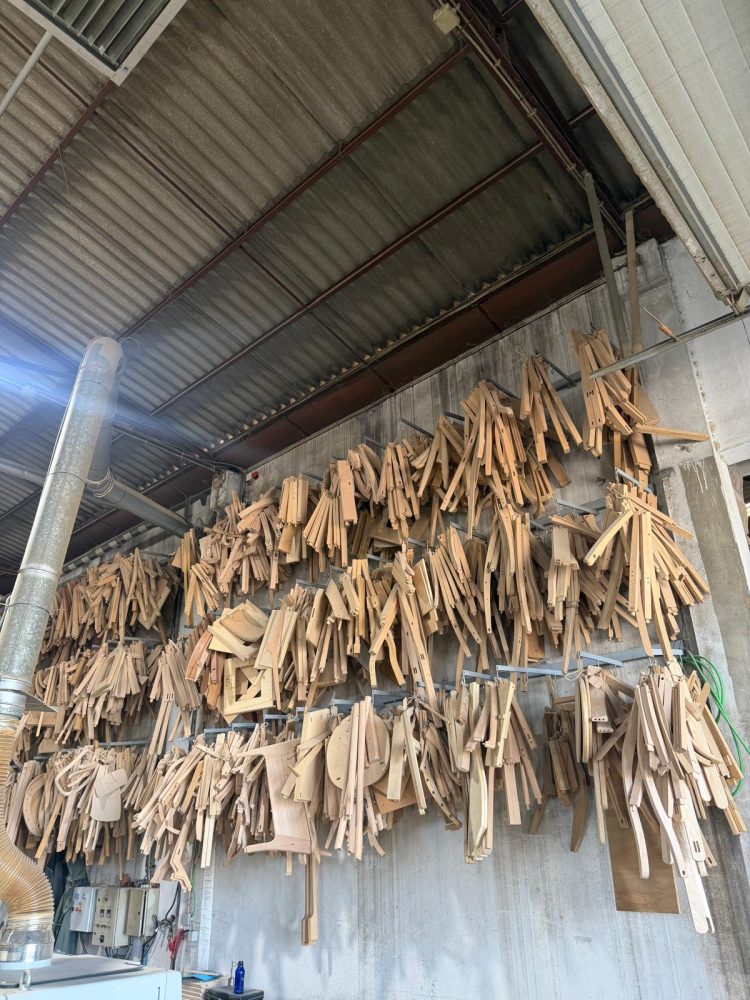 Photo of lots of pieces of wood resembling chair legs and other pieces hanging on the wall of an industrial building.